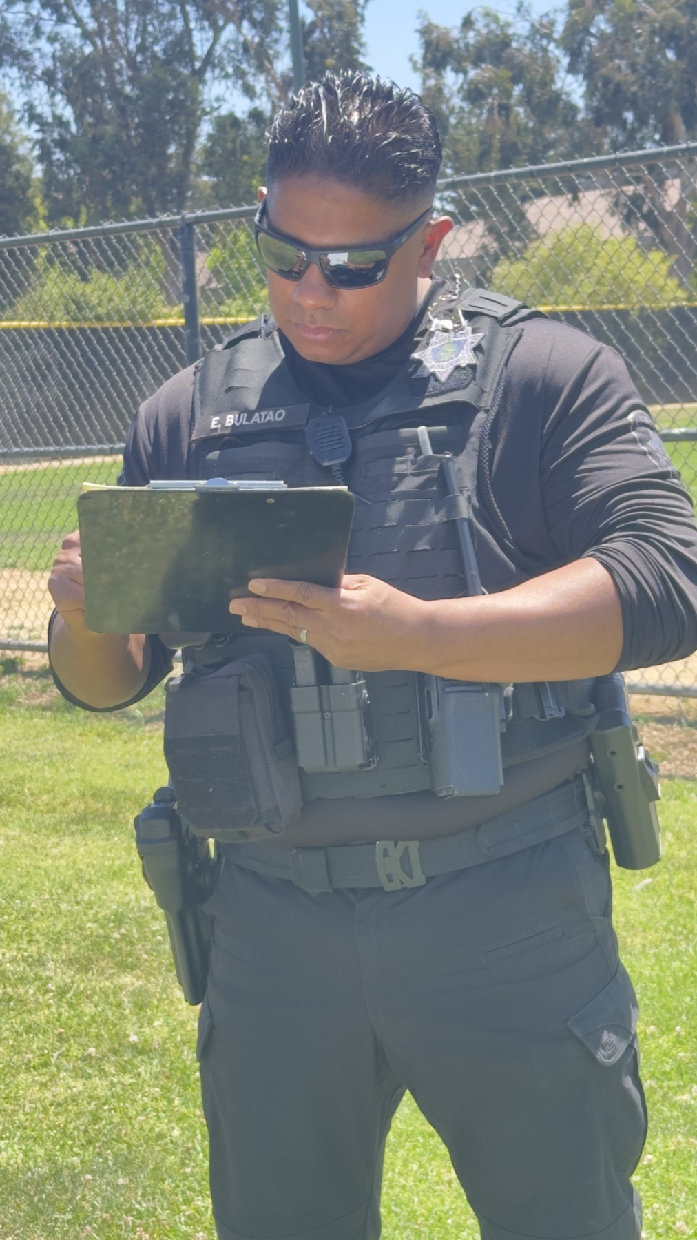 A Palo Alto police officer identified by uniform name tape as E. Bulatao writing on a clipboard