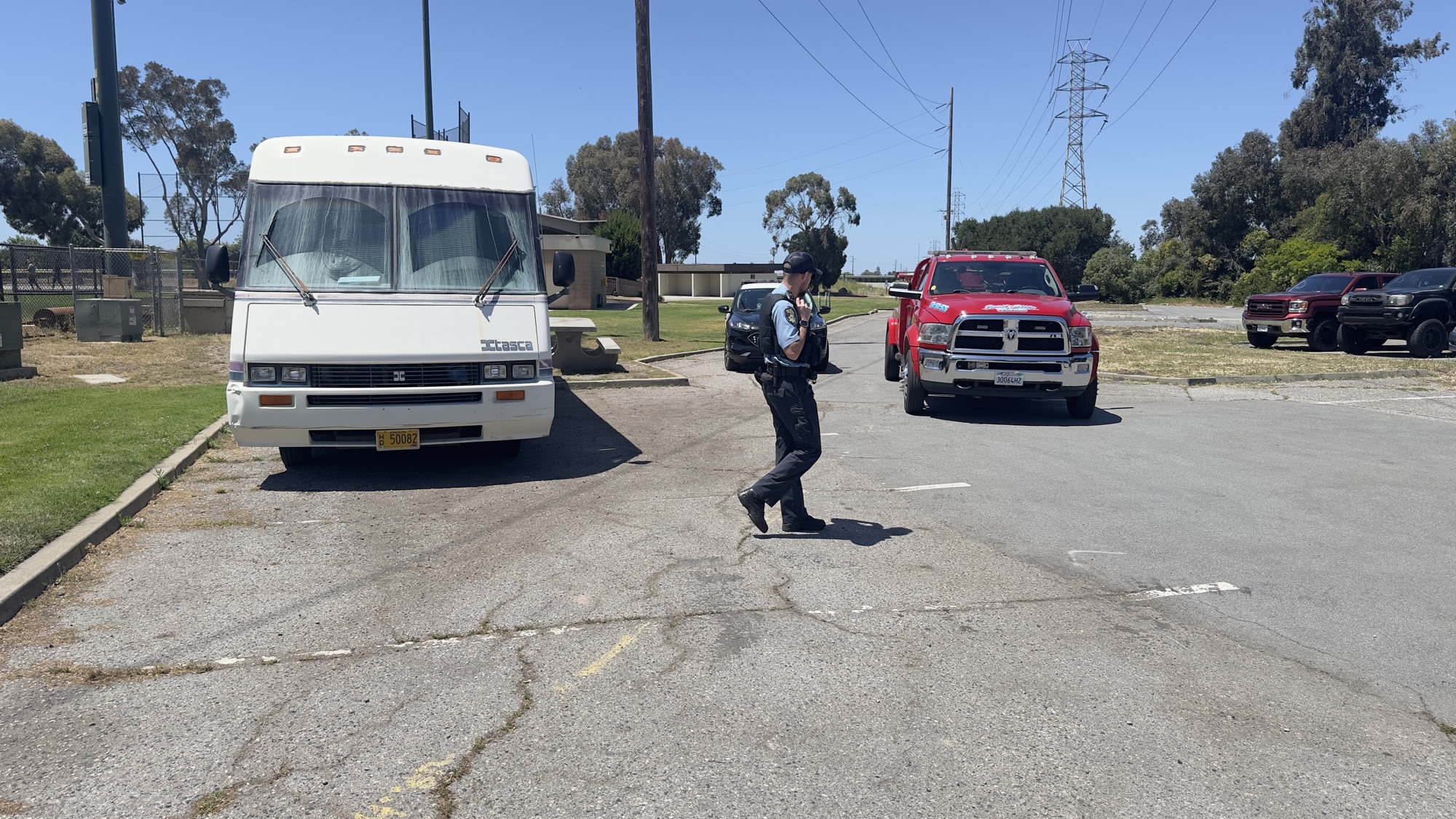 Wide view of an RV, officer, and tow truck in a parking lot on June 1, 2026